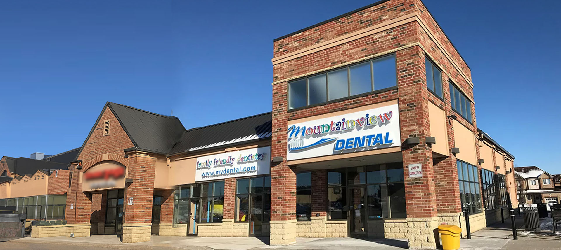In the image, a man wearing a blue coat is kneeling down next to three children who are sitting on the floor, all looking at something in his hands.